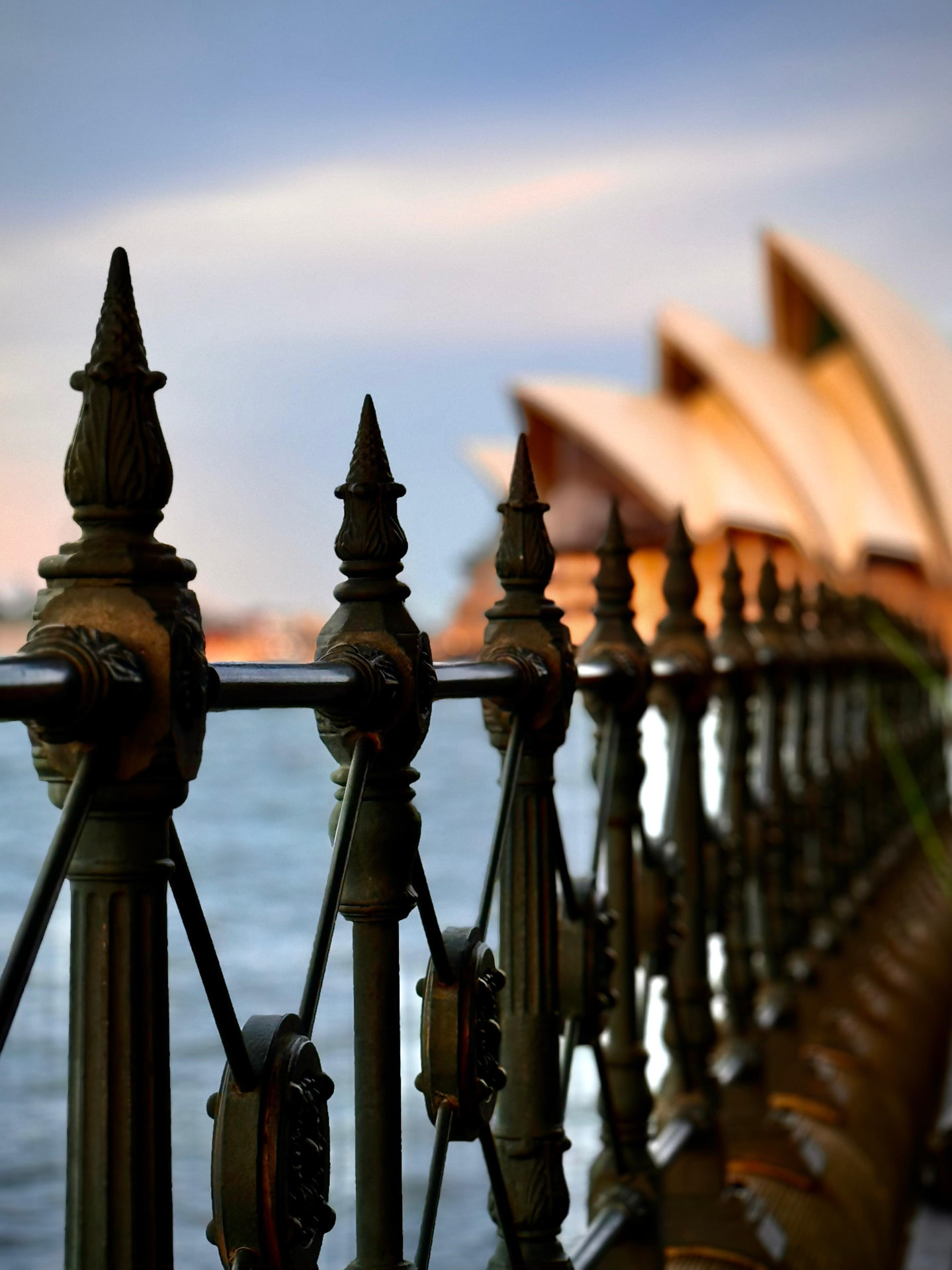 Ópera de Sydney desfocada ao fundo, vista através das lanças de um gradeado de ferro em primeiro plano