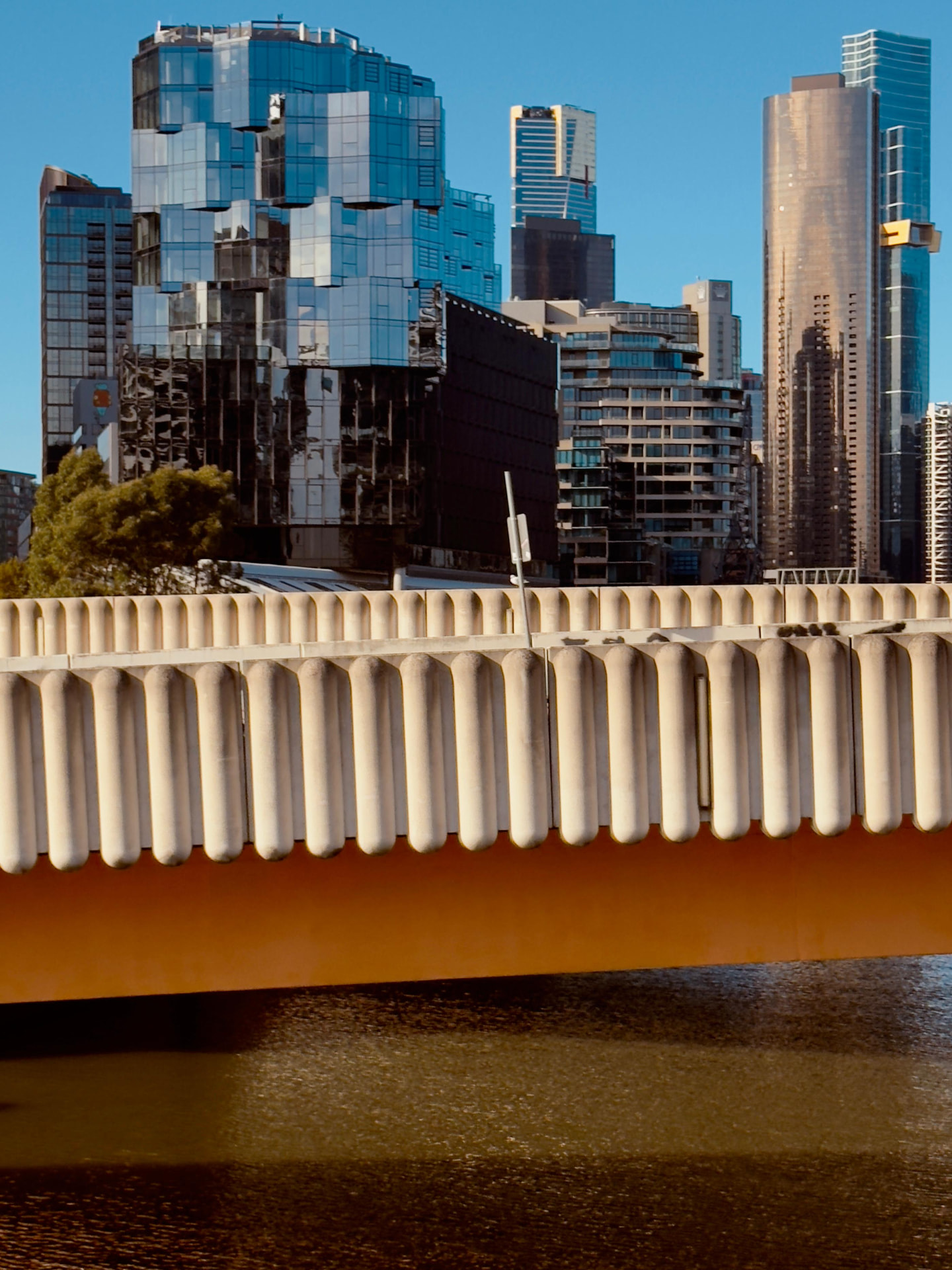 Ponte laranja com guarda-corpo de concreto em primeiro plano e arranha-céus de Melbourne ao fundo